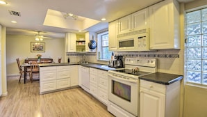 A kitchen with white cabinets, a microwave, an oven, and a dining area with a table and chairs.