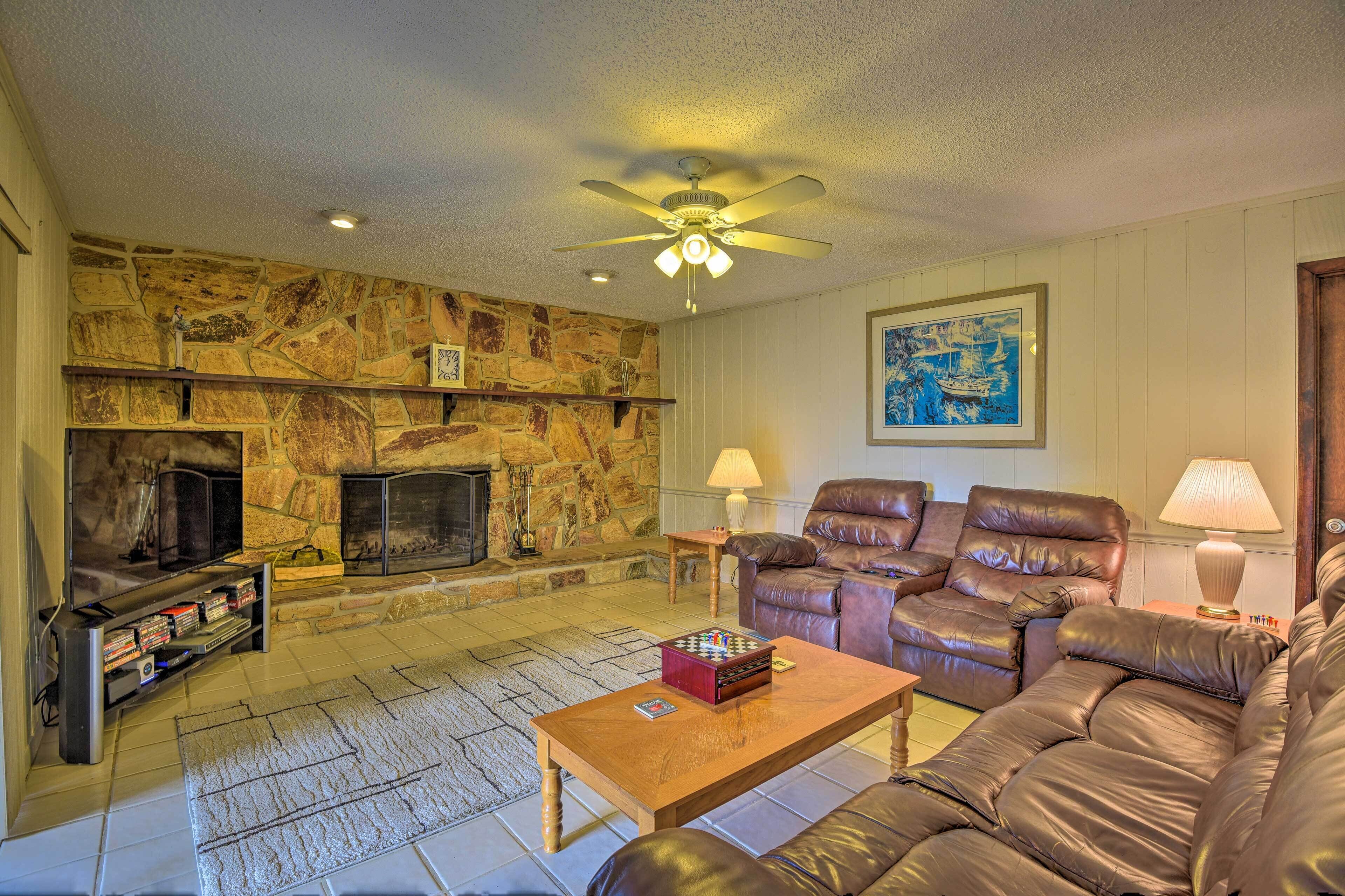 A living room with a stone fireplace, leather sofas, a wooden coffee table, and a ceiling fan.