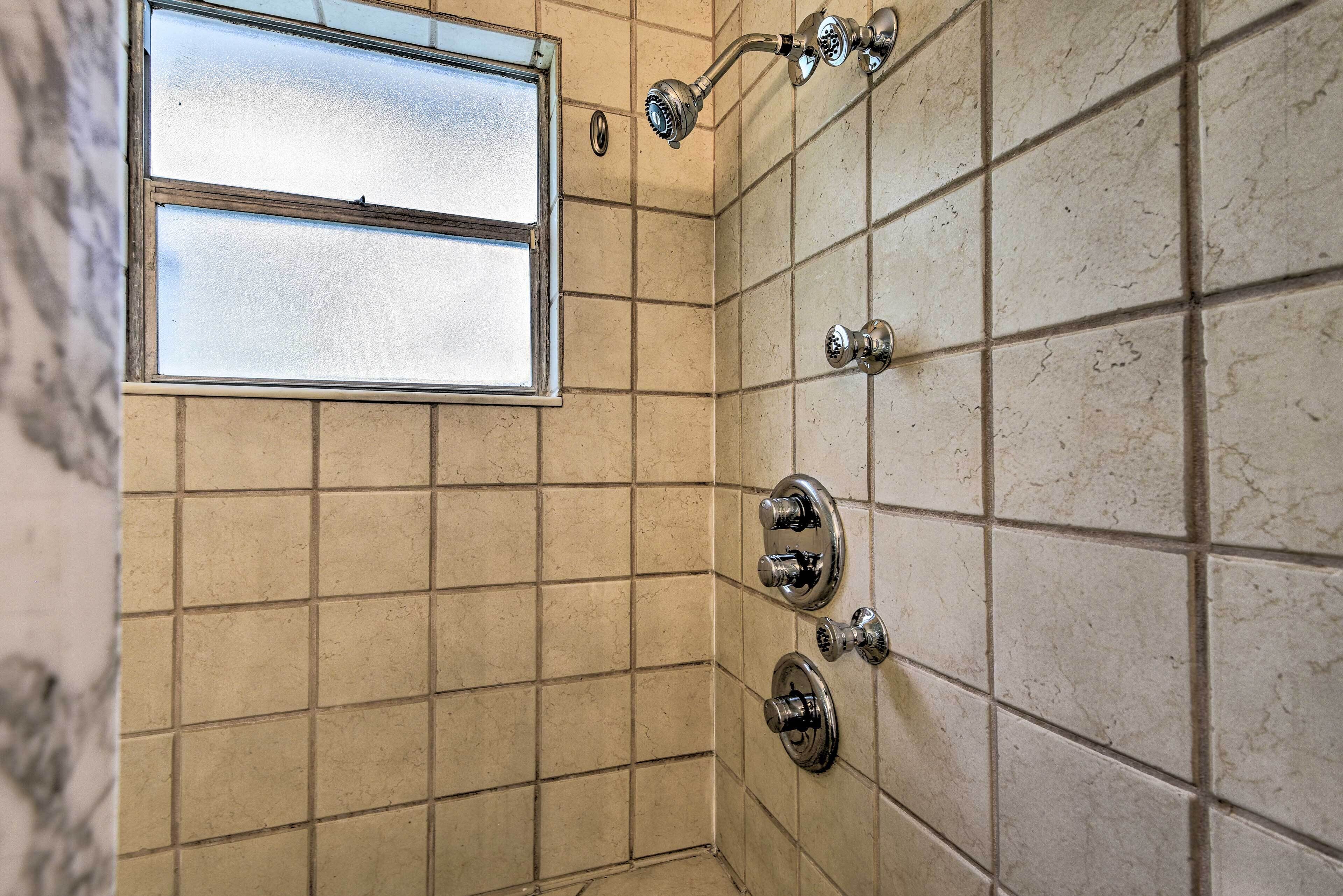 Un baño con paredes de azulejos color crema, una ventana y una ducha con accesorios cromados.