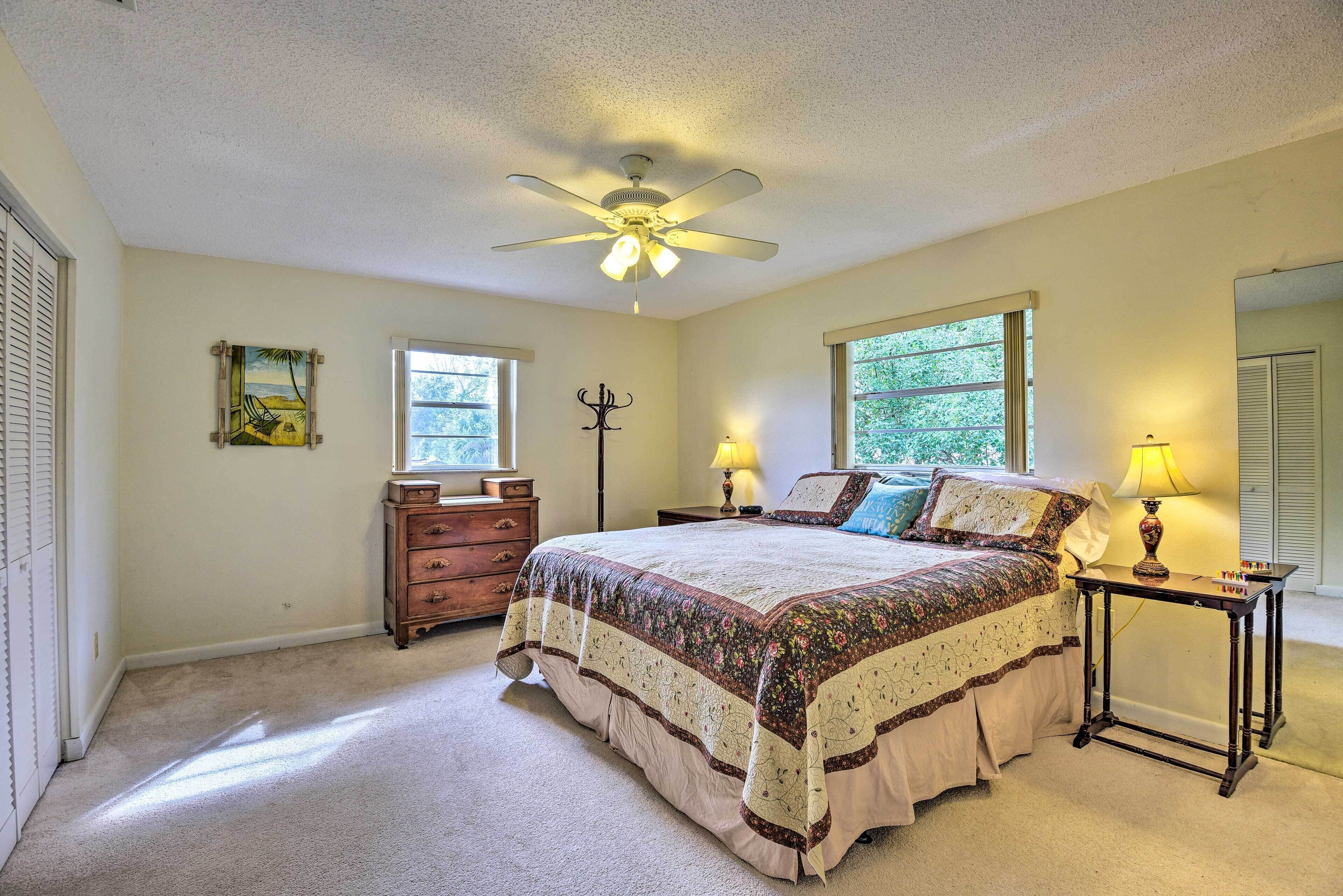 Une chambre à coucher comprenant un lit, un ventilateur de plafond, une commode, deux tables de chevet avec des lampes et une fenêtre.