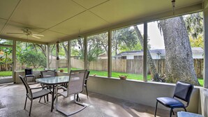 A covered patio with a table and chairs, large windows, and a view of a backyard.