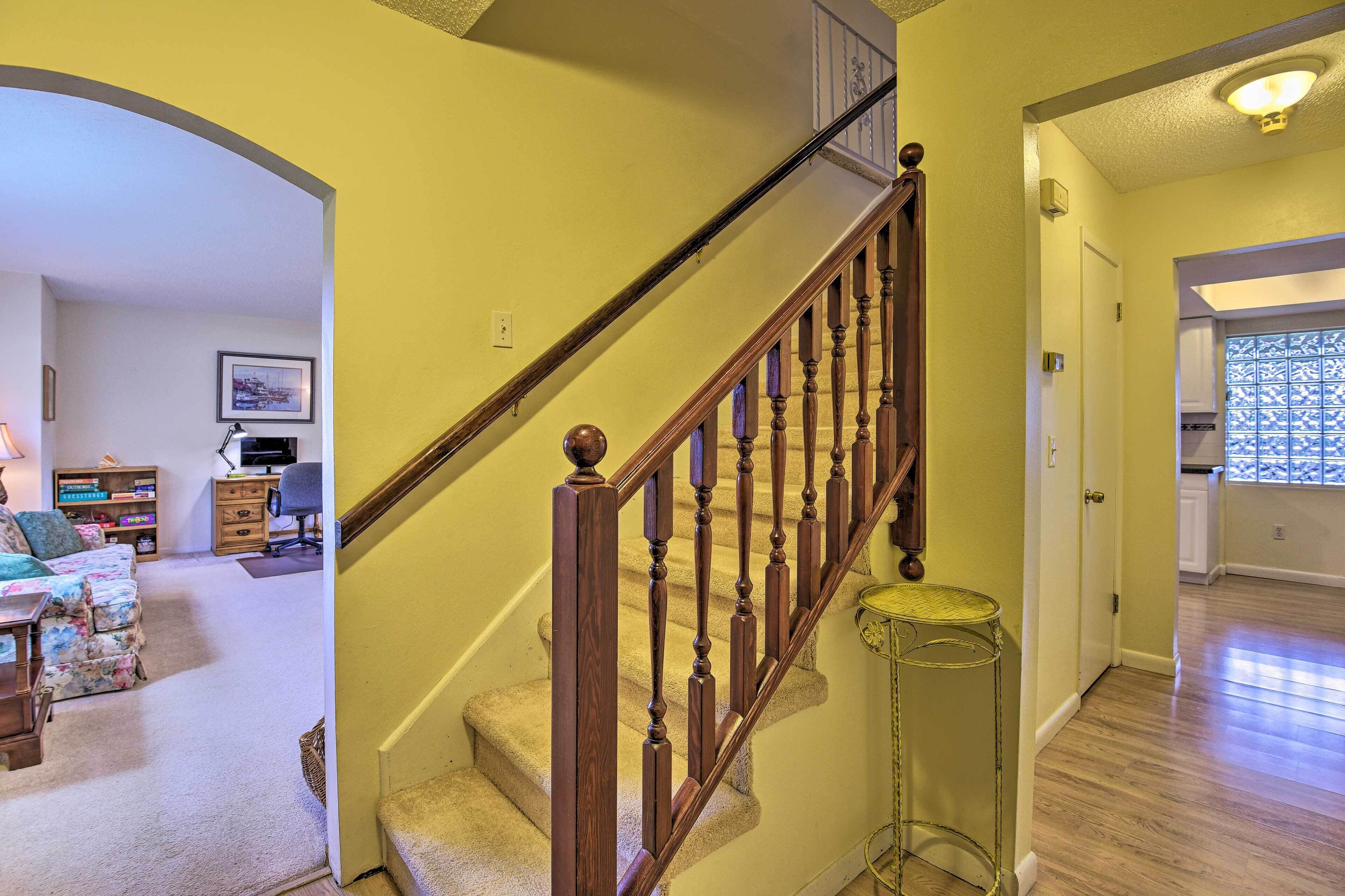 Un escalier avec des balustrades en bois menant à un deuxième étage, une petite table ronde placée à côté de l’escalier et une porte donnant sur un espace cuisine.