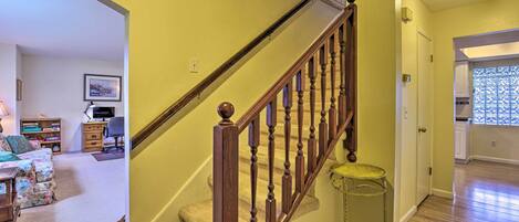 Un escalier avec des balustrades en bois menant à un deuxième étage, une petite table ronde placée à côté de l’escalier et une porte donnant sur un espace cuisine.