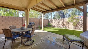 Une terrasse extérieure avec une table ronde et des chaises, un barbecue et une petite pelouse.