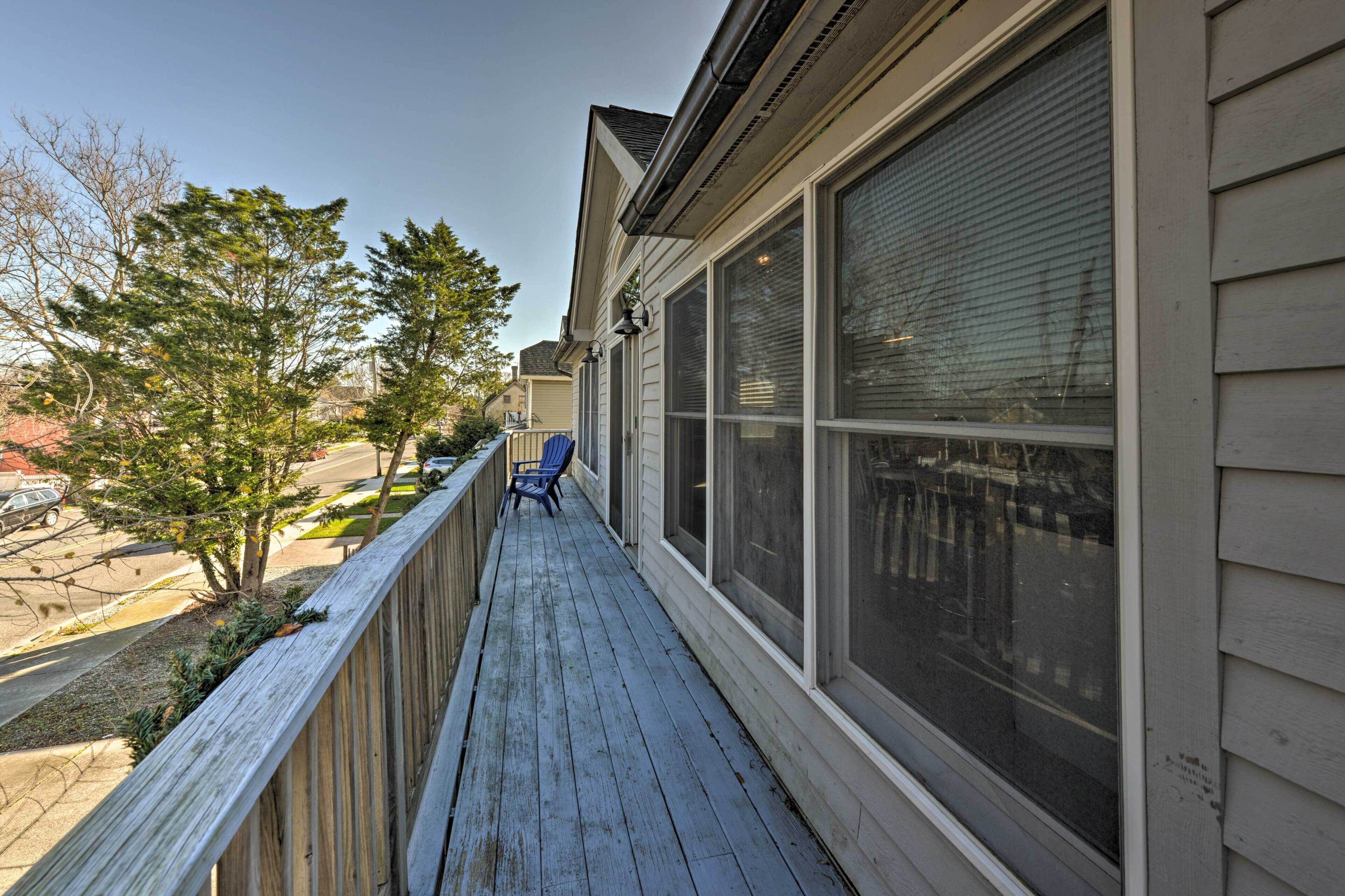 A wooden deck with a blue chair, large windows, and a view of the street and trees.
