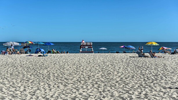 Een strand met een bewakerspost, parasols en mensen die ontspannen.