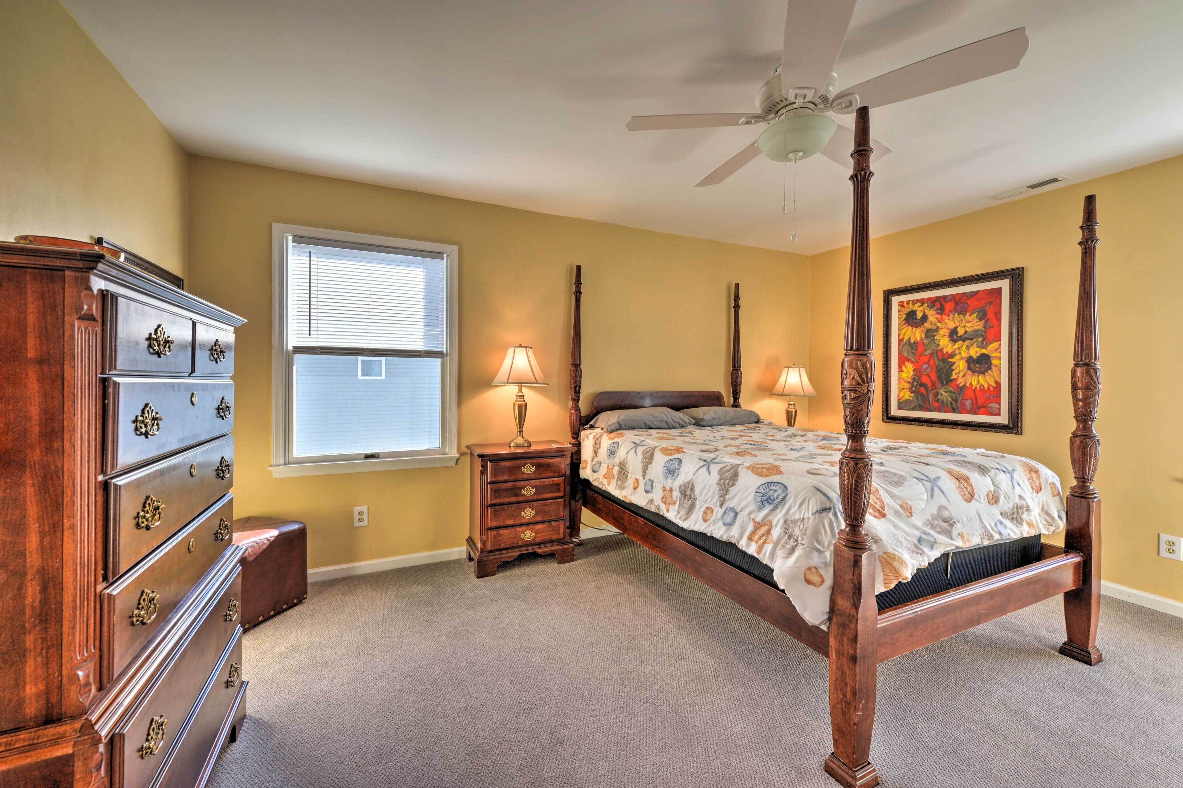 A bedroom with a four-poster bed, a wooden dresser, a nightstand with lamps, and a window with blinds.