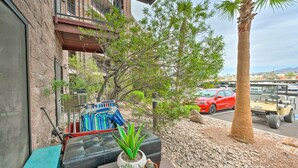 A patio with a black leather bench, a small table with potted plants, and a view of a red car and a yellow vehicle on the street. - Walk to Beach: Lake Havasu Condo w/ Pool Access (Lake Havasu City)