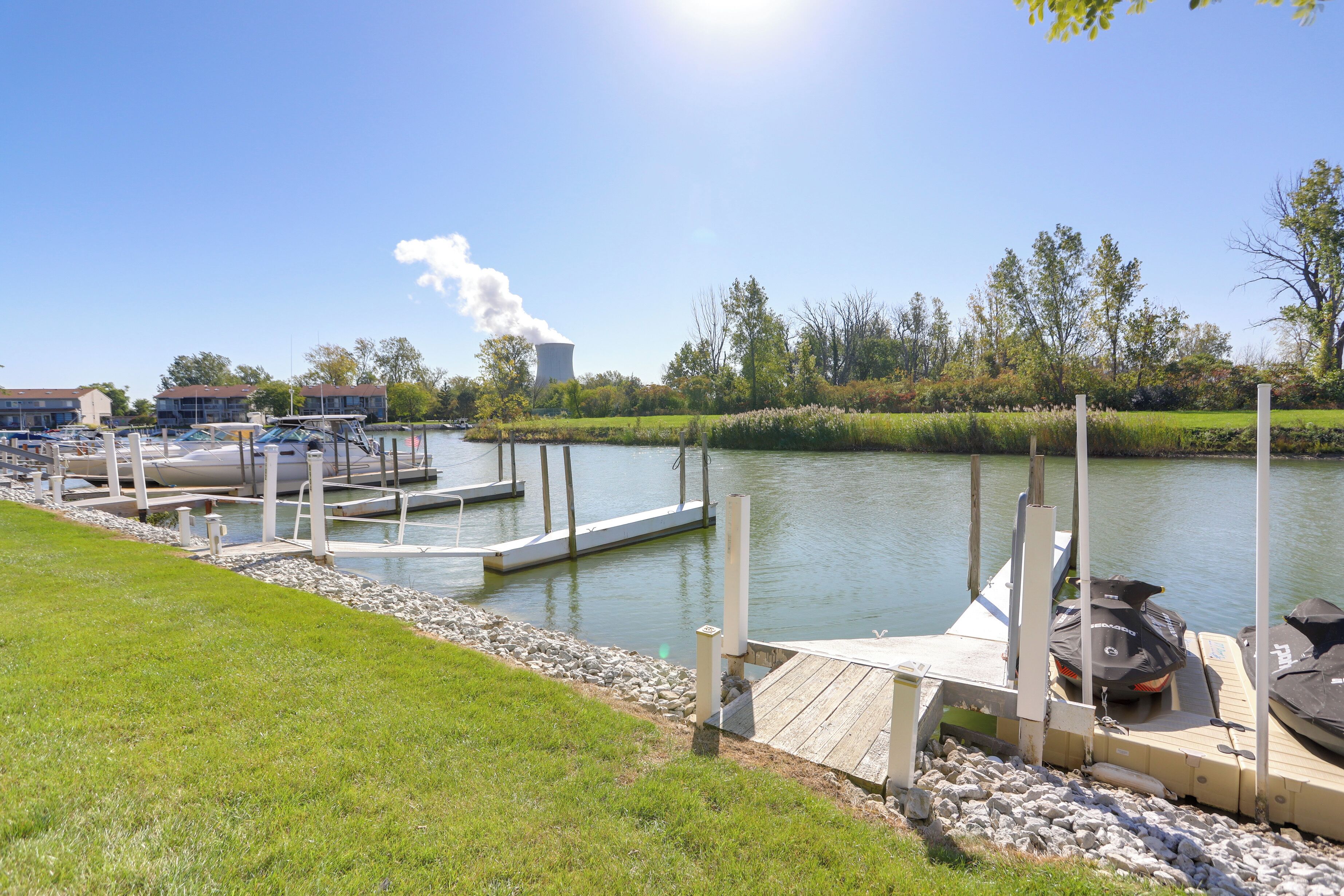 A marina with docked boats, a grassy area, and a cooling tower in the background.