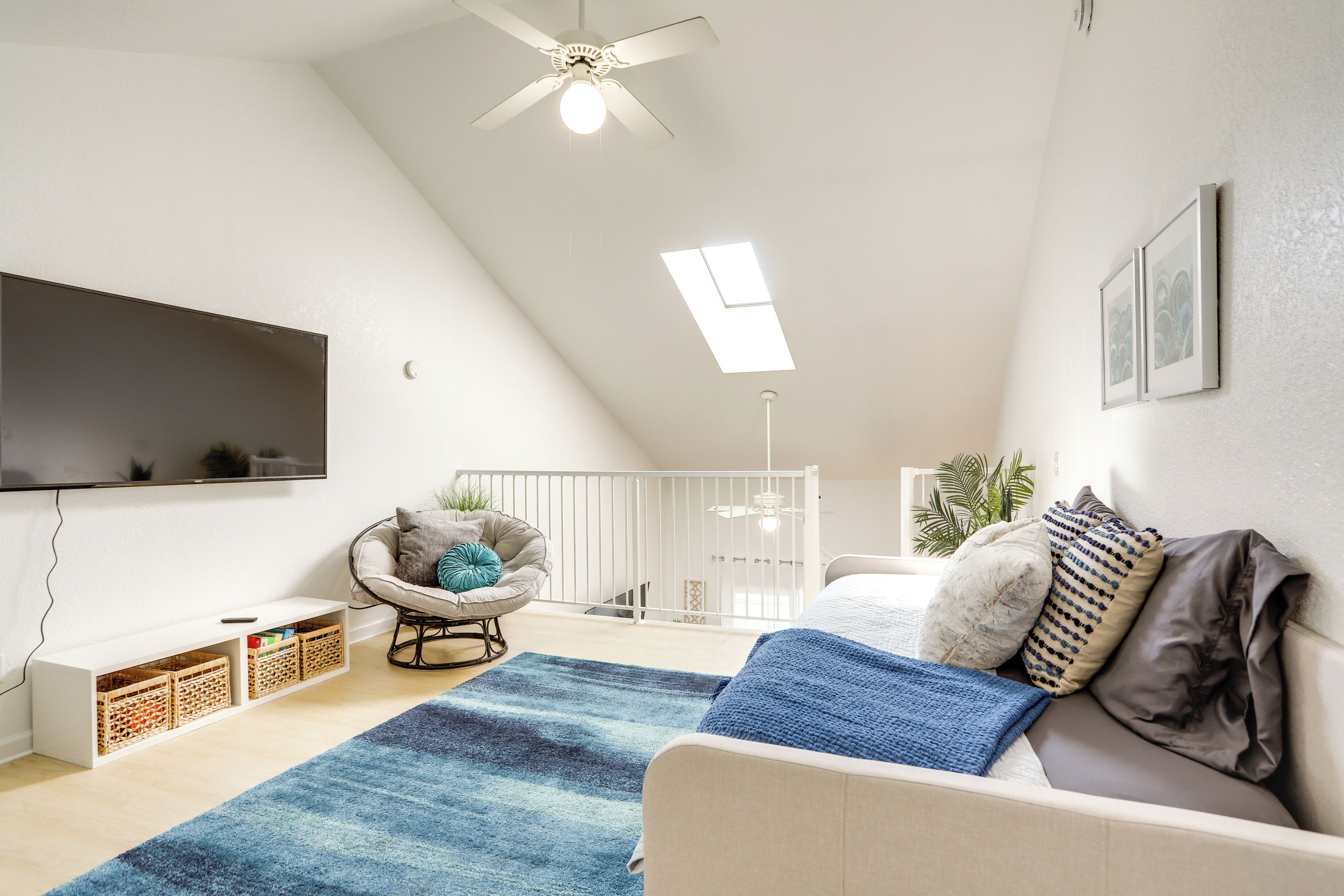 Un salon moderne doté d’un ventilateur de plafond, d’un téléviseur à écran plat, d’un canapé, d’un fauteuil et d’une petite table avec des bacs de rangement.