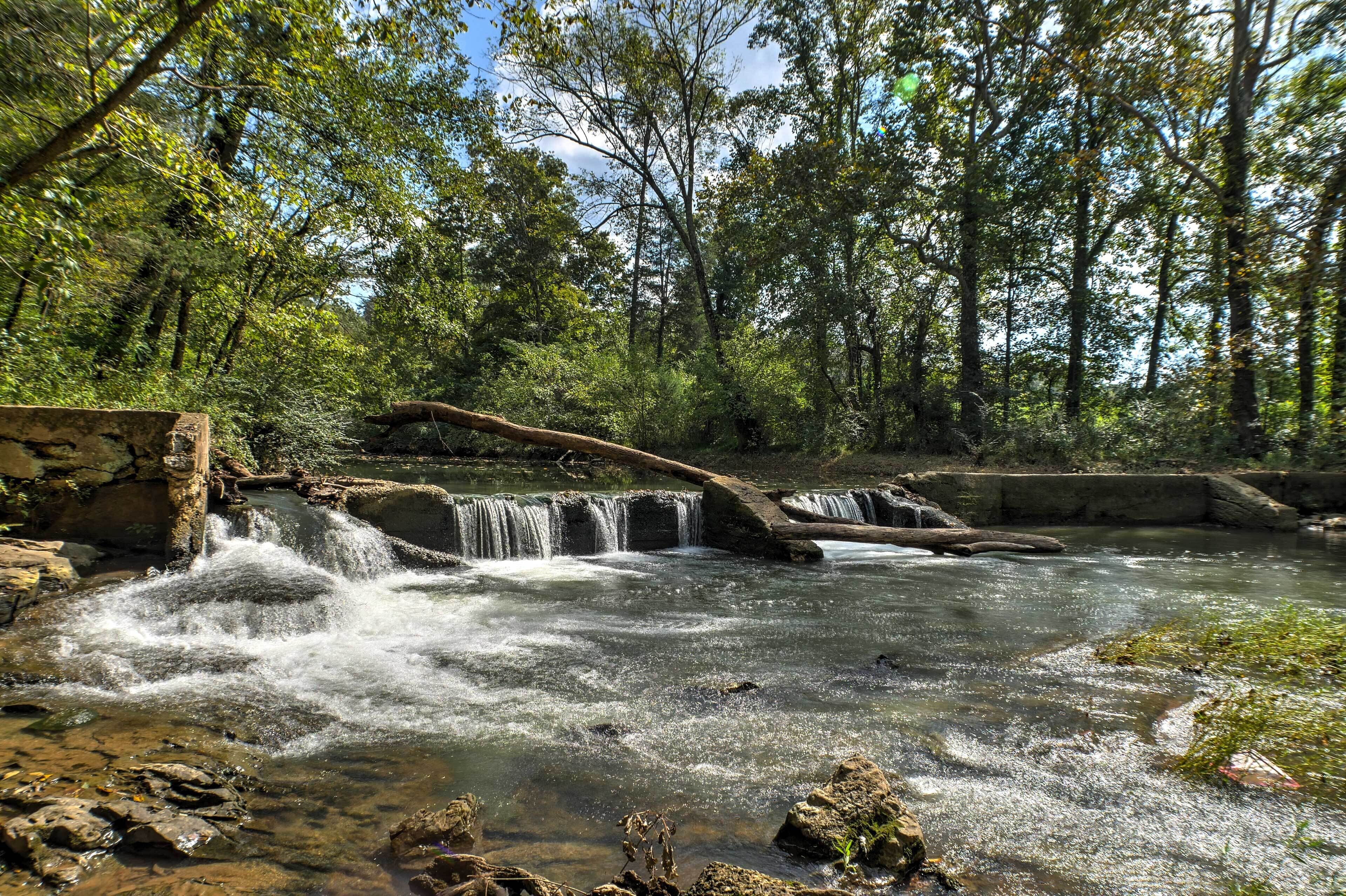 A natural waterfall in a forested area with a stone bridge.