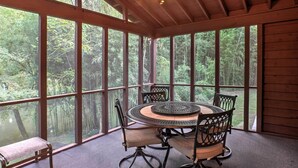 A covered patio with a round table and chairs, large windows, and a ceiling fan. - Creekfront Cabin Near Chattanooga w/ Hot Tub! (Ooltewah)