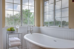 A bathroom with a freestanding bathtub, a towel rack with folded towels, and a window with a view of trees. - 'fox Ridge Farmhouse' - Hill Country Getaway! (San Marcos)