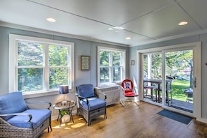 A sunlit room with large windows, wicker furniture, and a view of the outdoors.