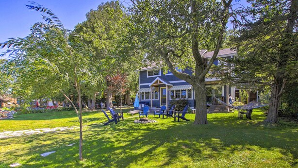A two-story house with a covered porch, a lawn with outdoor furniture, and trees. - Crystal Lake Cottage: Kayaks & Fire Pit! (Plymouth)