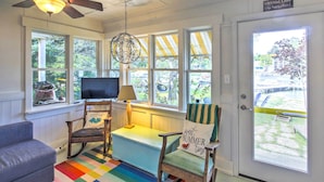 A cozy room with a ceiling fan, a television, a rocking chair, a bench, and a colorful rug. - Crystal Lake Cottage: Kayaks & Fire Pit! (Plymouth)