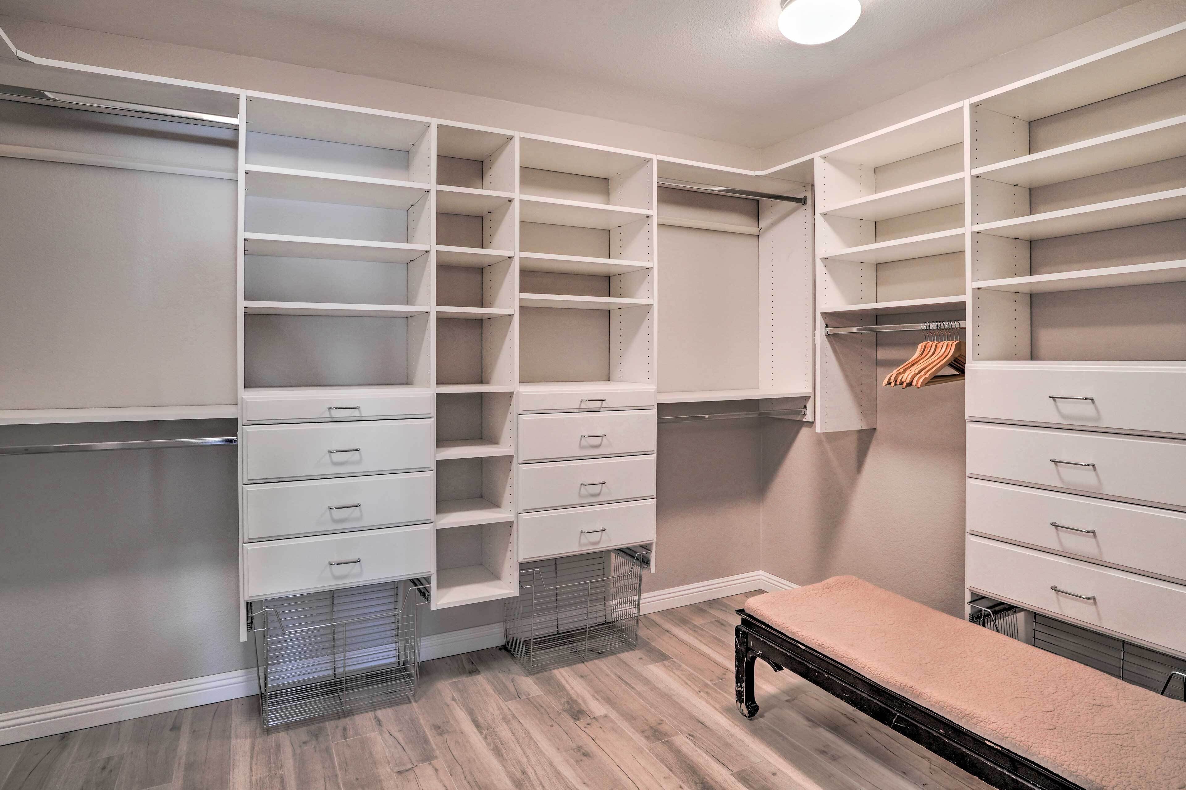 A walk-in closet with multiple shelves and drawers, a bench, and a hanging rod.