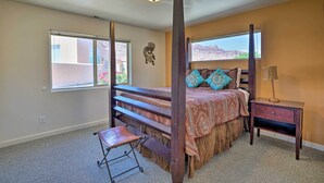 A bedroom with a four-poster bed, a small bedside table, a chair, and a window with a view of a desert landscape. - Moab Townhome w/ Pool Access + Stunning Mtn Views! (Moab)