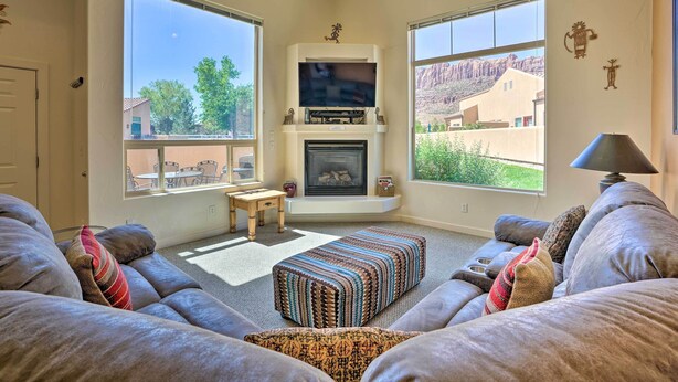 A living room with a fireplace, large windows, and a sofa. - Moab Townhome w/ Pool Access + Stunning Mtn Views! (Moab)