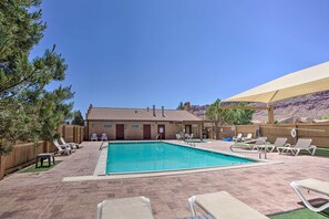 A swimming pool with lounge chairs, a wooden fence, and a building with a tiled roof. - Moab Townhome w/ Pool Access + Stunning Mtn Views! (Moab)