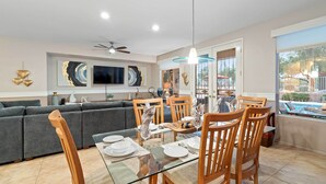 A dining area with a glass table, wooden chairs, and a grey sofa in the background. - Sun City Grand Golf Course Gem w/ Pool, Spa & Cart (Surprise)
