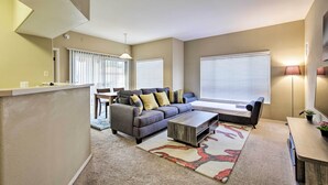 A modern living room with a grey sofa, a coffee table, and a rug. There is a dining area with a table and chairs in the background. - Condo w/ Pool Access, 5 Mi to Tempe Diablo Stadium (Tempe)