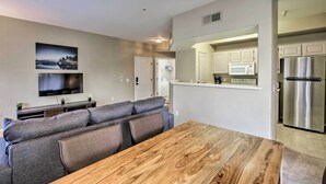 A modern living room with a wooden dining table, grey sofas, a flat-screen TV, and a kitchen area with a refrigerator and microwave. - Condo w/ Pool Access, 5 Mi to Tempe Diablo Stadium (Tempe)