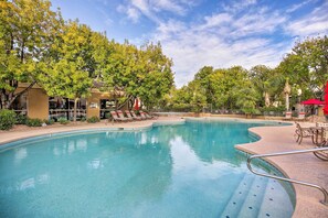 Une piscine entourée d’arbres et de bâtiments, avec des chaises longues et des parasols.