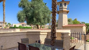 A patio with a glass table and chairs, a palm tree, and a lighthouse in the background.