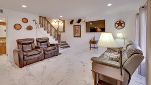 A spacious living area with a marble floor, leather sofas, a staircase, and a flat-screen TV.