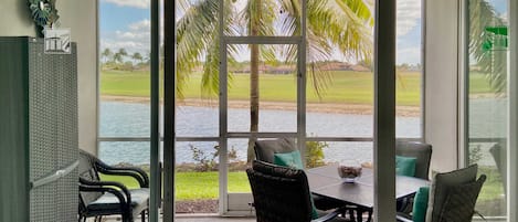 A room with a large sliding glass door leading to a view of a golf course and water. Inside, there is a table with chairs, a ceiling fan, and a decorative star on the wall.