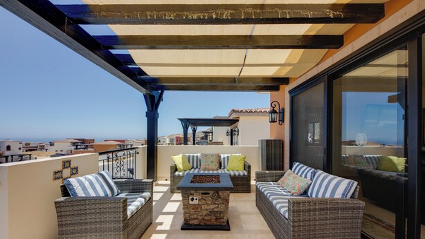 Un balcone con mobili in vimini, un tavolo in pietra e vista sul mare.