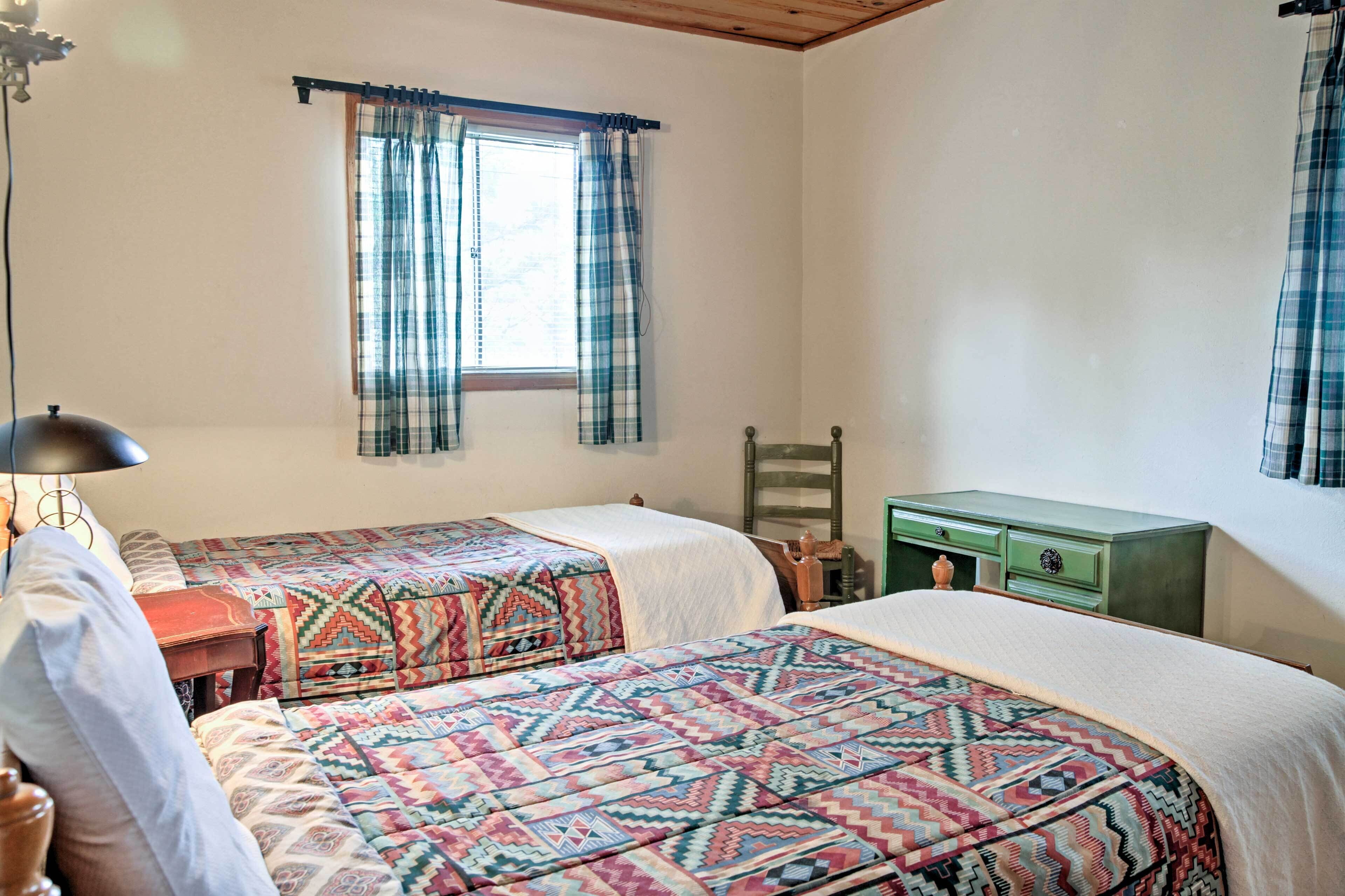 A bedroom with two beds, a green dresser, a wooden chair, and a window with plaid curtains.