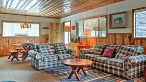 A cozy living room with plaid sofas, a wooden ceiling, and large windows with blinds. - Ruidoso Log Cabin Near Skiing & Wildlife! (Ruidoso)