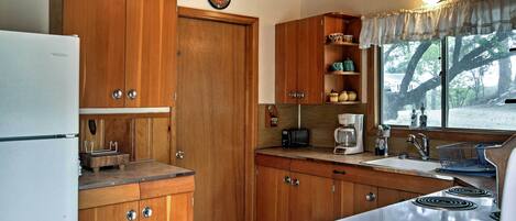 A kitchen with wooden cabinets, a white refrigerator, a stove, and a window with a view of trees.