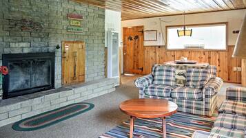 A cozy living room with a fireplace, plaid furniture, and a wooden ceiling.