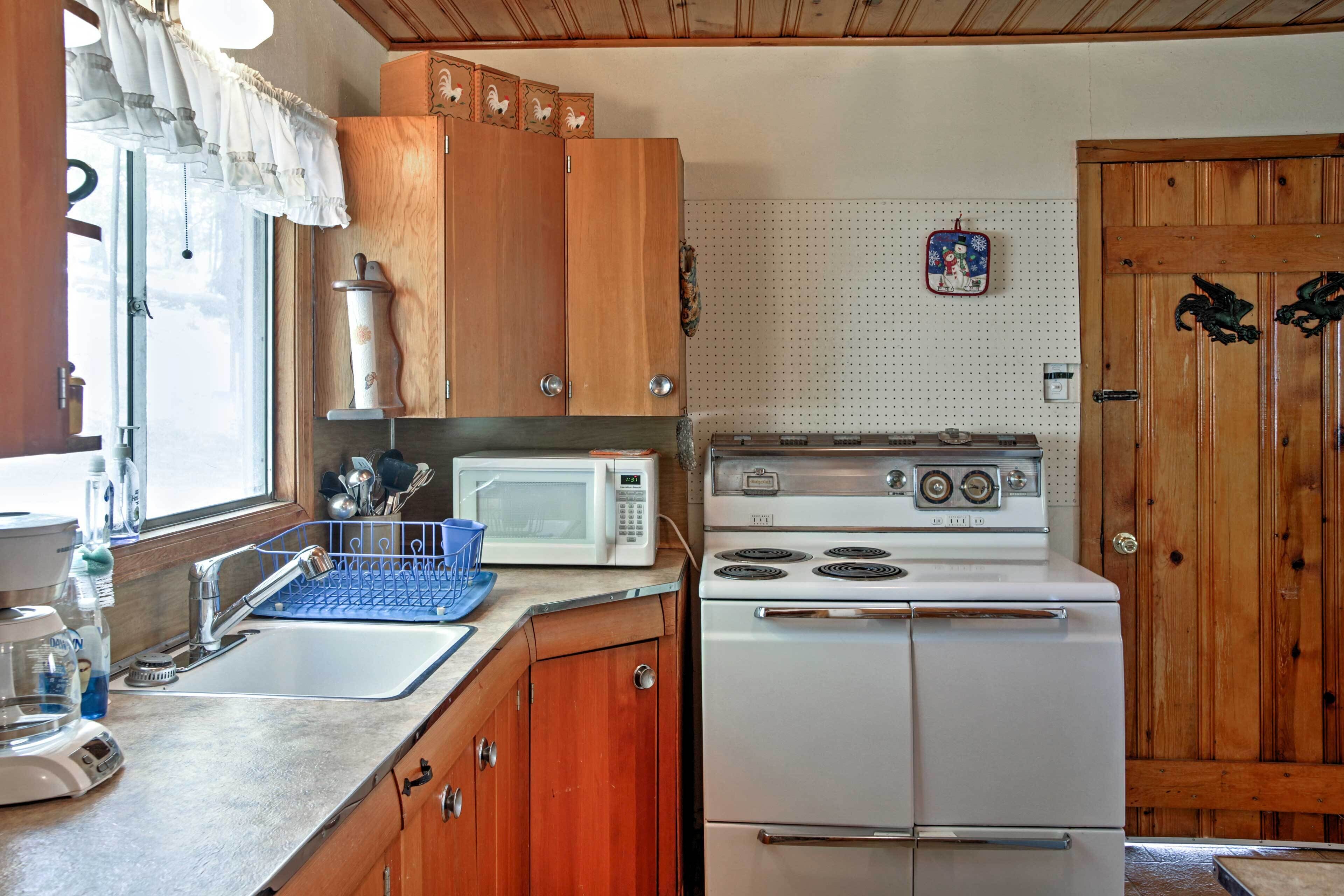 A kitchen with wooden cabinets, a white stove, a microwave, and a sink.
