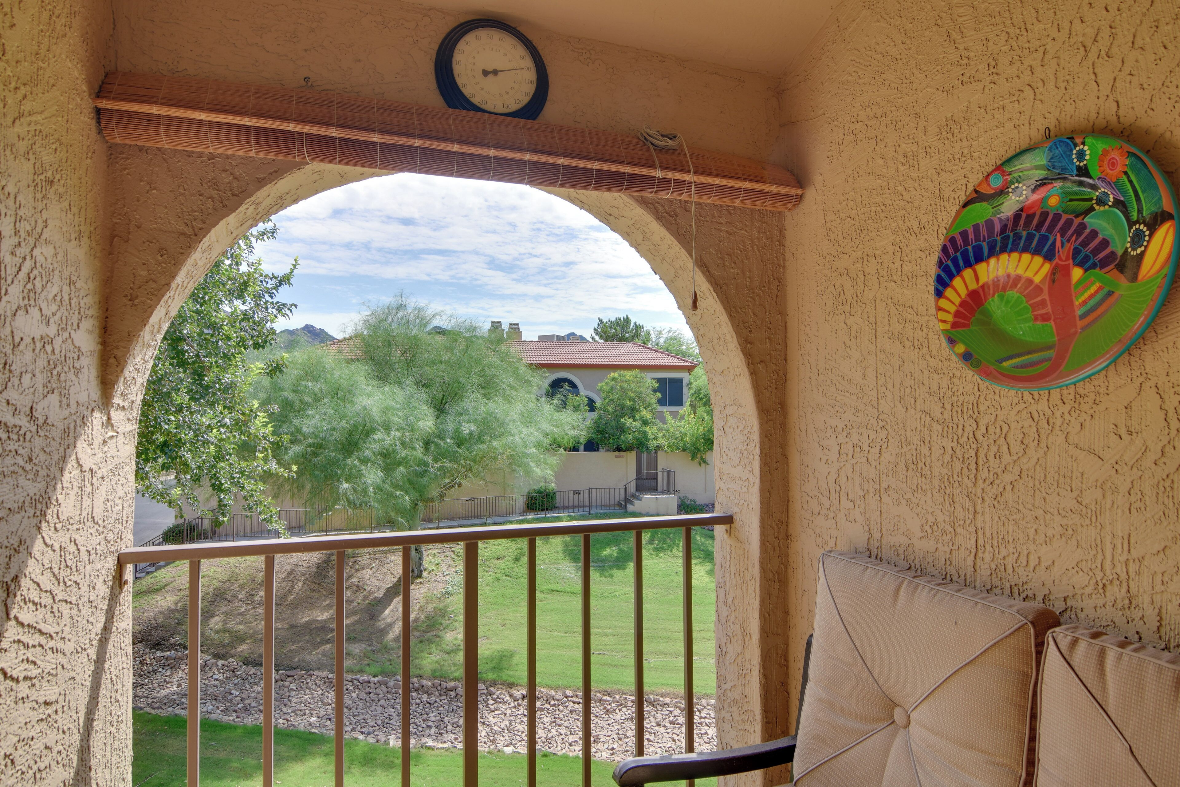 A balcony with a view of a house, a clock, and a colorful wall decoration.