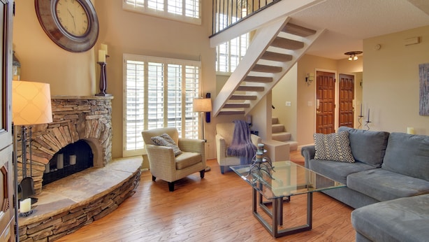 A spacious living room with a stone fireplace, a glass coffee table, a sofa, and a staircase leading to an upper level. - North Phoenix Gem w/ Courtyard & Pool Access (Phoenix)