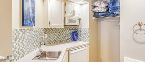Cocina compacta con armarios blancos, microondas y pileta.