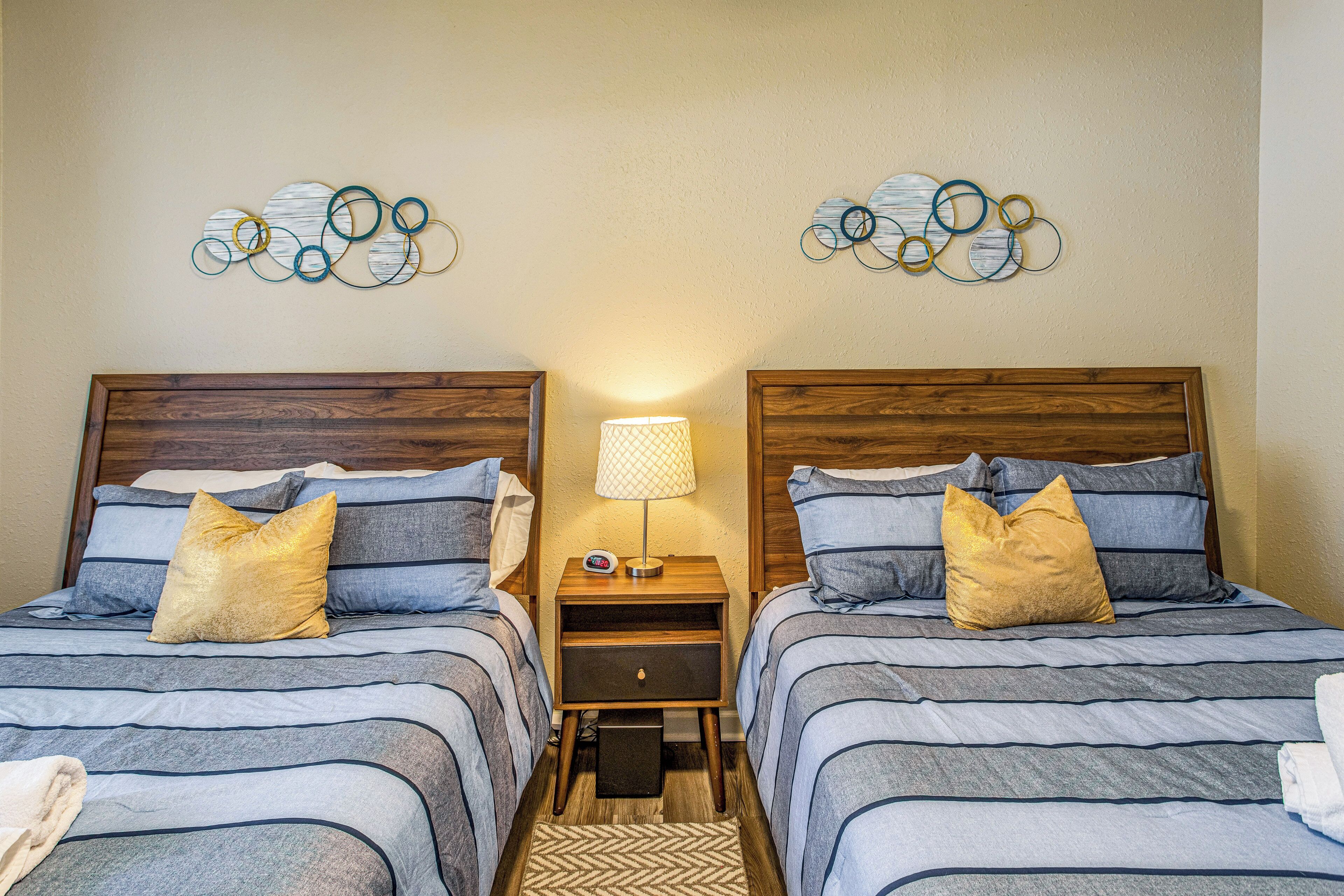 A hotel room with two beds, each with a wooden headboard, a nightstand with a lamp, and decorative wall art.