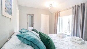 A hotel room with a large bed, a mirror, a window with curtains, and a painting on the wall. - Donnys Plaice (Great Yarmouth)