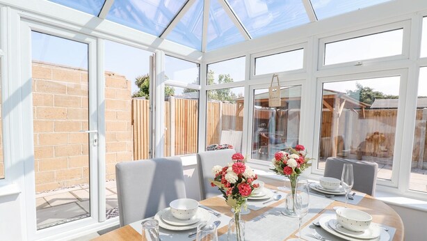 A conservatory with a dining table set for four, surrounded by large windows and a view of a brick wall and garden. - Donnys Plaice (Great Yarmouth)