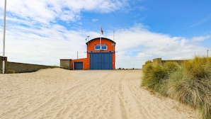 A sandy beach leading to a red building with a blue door and a flag on top. - Donnys Plaice (Great Yarmouth)