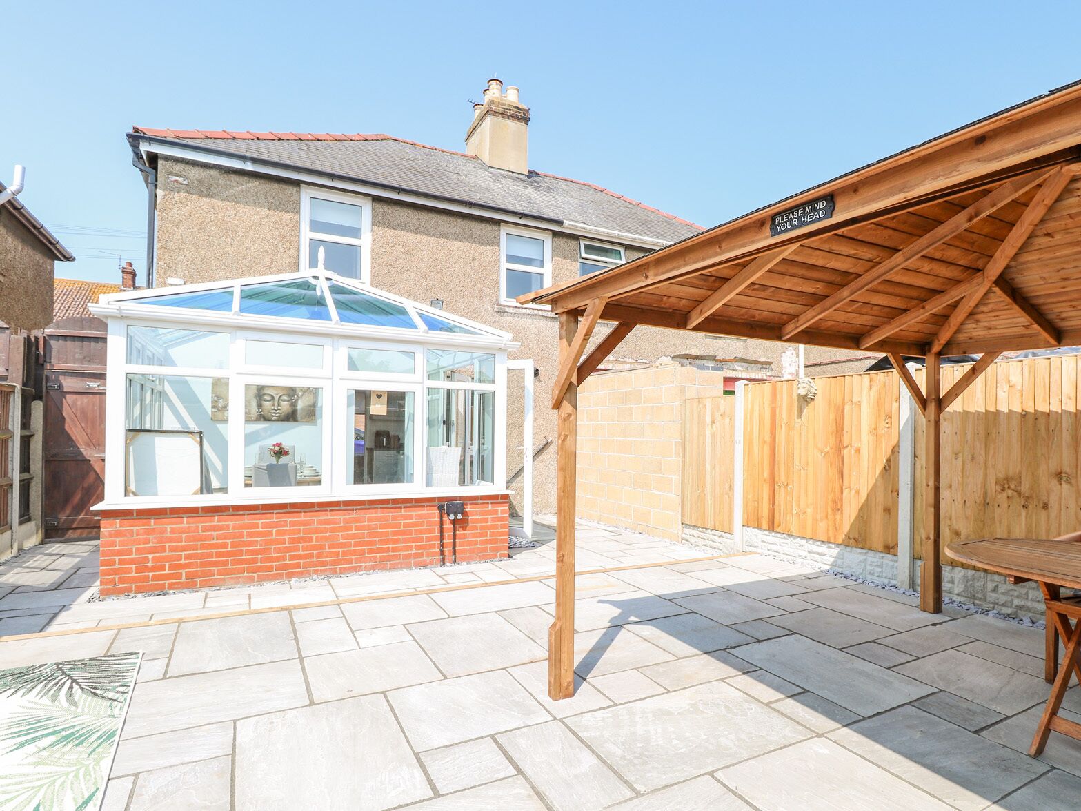 A conservatory with a glass roof, a wooden pergola, and a tiled patio.