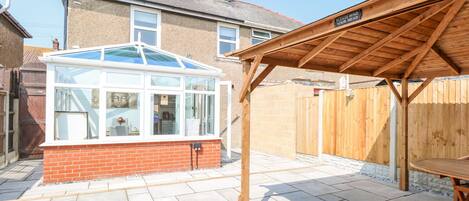 A conservatory with a glass roof, a wooden pergola, and a tiled patio.