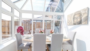 A conservatory with a dining table set for four, surrounded by chairs, and a large window offering a view of the outside. - Donnys Plaice (Great Yarmouth)