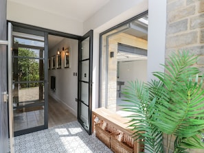 A hallway with a patterned floor, a wooden bench with baskets, and a large potted plant. - Greystones (Gloucester)
