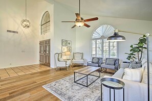 A spacious living room with hardwood flooring, a ceiling fan, a large window with blinds, a sofa, two armchairs, a coffee table, and a floor lamp. - Upscale Phoenix Abode: Walk to South Mountain Park (Phoenix)