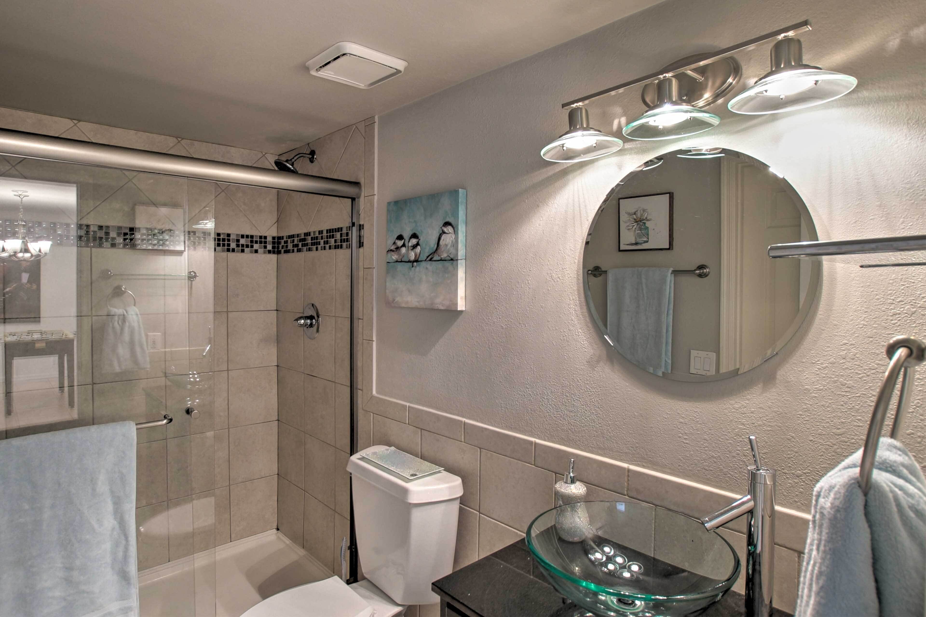 A modern bathroom with a glass-enclosed shower, a round mirror, and a glass bowl sink.